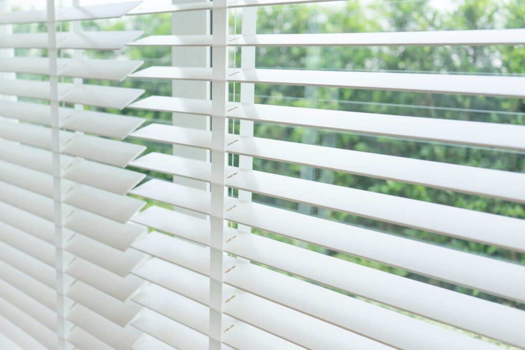 Close up of a window with white faux wood blinds